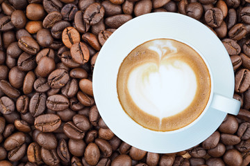 Hot latte coffee in white cup on coffee beans background, top view