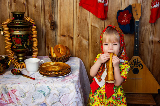 a little girl in russian folk clothes at the celebration of the slavic holiday of maslenitsa eats traditional russian treats