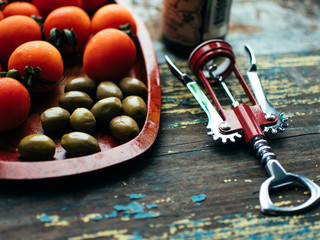 top view of bottle of red wine, corkscrew, green olives on wooden tabletop.