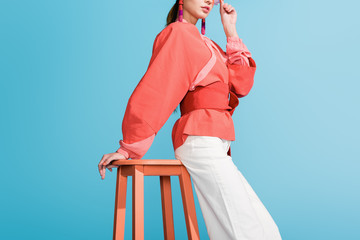cropped view of woman in trendy living coral clothing posing on stool isolated on blue