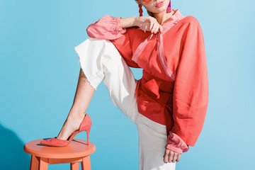 cropped view of girl in living coral clothing posing on stool on blue