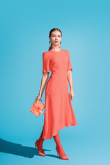 stylish woman in living coral dress holding gift box on blue