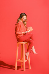 elegant young woman holding birthday present and sitting on stool on living coral