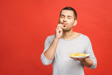 Young man holding french fries. Student eats fast food. Not helpful food. Very hungry guy. Diet concept. Isolated over red background.