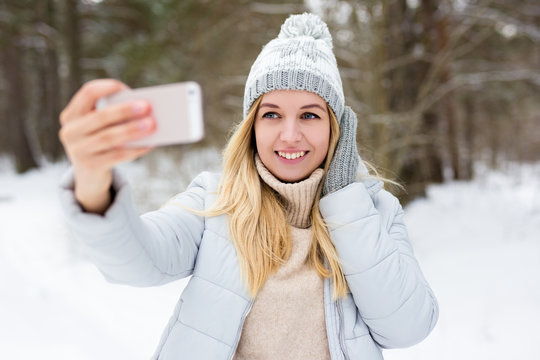 portrait of young blond woman taking selfie photo in winter park or forest