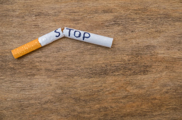 broken cigarette with the word stop on a wooden background; stop smoking close concept; space for text