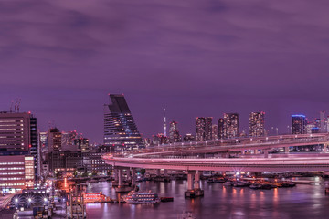Fototapeta na wymiar Purple night on circular highway leading to the Rainbow Bridge with Cargo and cruise ships moored or sailing in Odaiba Bay of Tokyo.