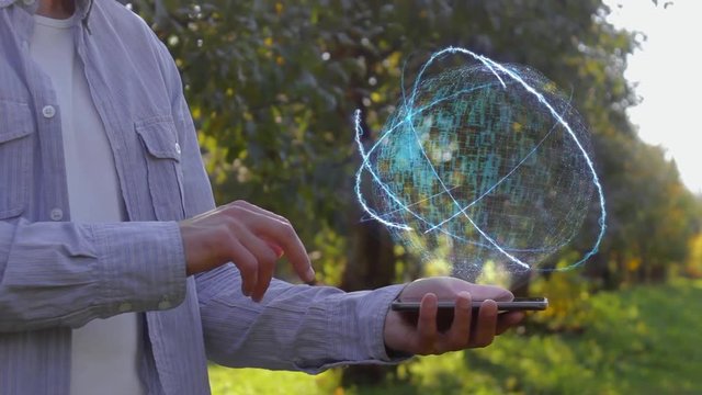 Unrecognizable man shows conceptual hologram with text Developer. Farmer on the background of the apple orchard in casual clothes with the technology of the future mobile screen