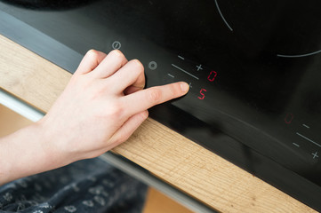 Dangerous situation in the kitchen. Child playing with electric glass-ceramic cooktop stove.
