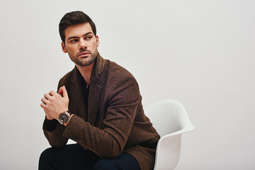 Confident in his style. Stylish dark-haired man sitting on a chair and looking at camera isolated...