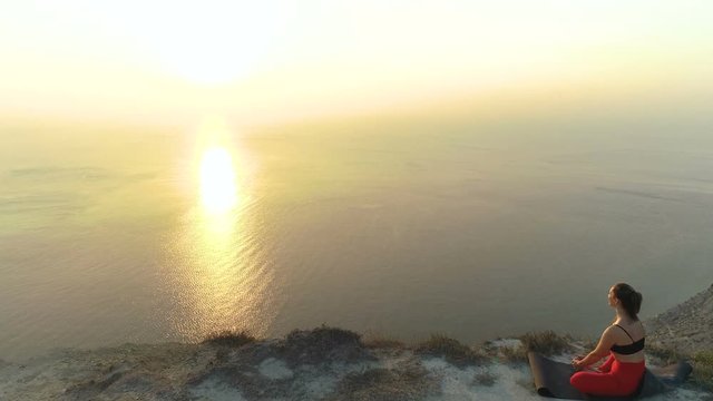 Beautiful view of woman doing yoga Baddha Konasana, Bound Angle Pose on the mountain with sea view at sunset.