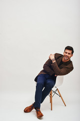 Success! Stylish dark-haired businessman sitting on a chair, leaning back, looking at camera and...