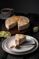 raw vegan cheesecake, on a wooden board, cup of tea and lime on a dark rustic backdrop