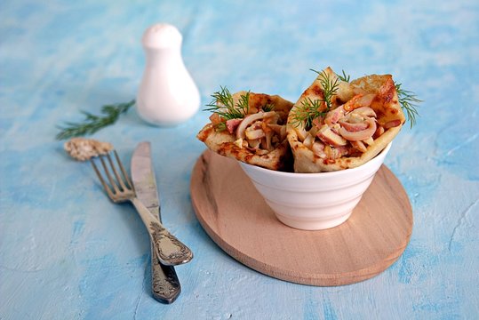 Thin pancakes stuffed with squid, roasted carrots and eggs on a light blue background. Served portions in white bowls, decorated with dill sprigs.