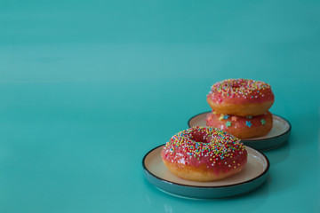 Pink glazed doughnuts with sprinkles on turquoise background