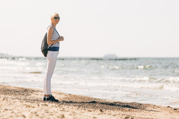 Young, beautiful blonde girl walking at the beach. Stylish woman in white pants and sunglasses near sea