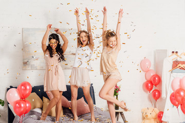 beautiful multicultural girls in nightwear dancing and having fun under falling confetti during pajama party