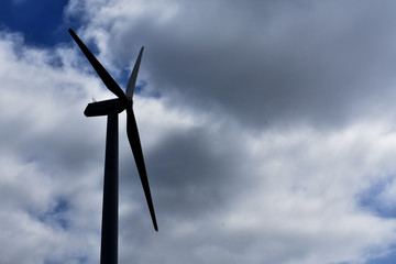 Silhouette wind turbine against cloudy sky.