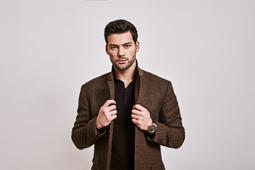 Looking just perfect. Stylish dark-haired man holding his jacket and looking at camera isolated...
