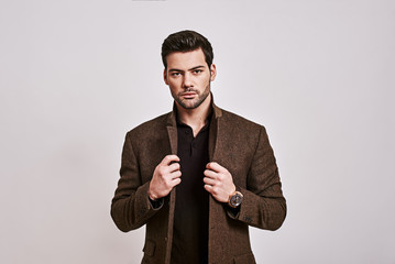 Looking just perfect. Stylish dark-haired man holding his jacket and looking at camera isolated over grey background