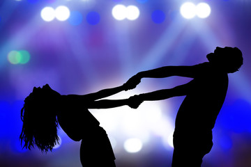 Silhouettes of a young couple dancing at live concert.