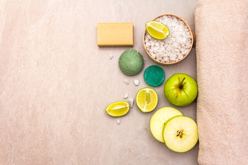 Spa concept, natural ingredients. Bath towel, sea salt with lime, apple, olive and mint soap, sponge. On a stone background, top view