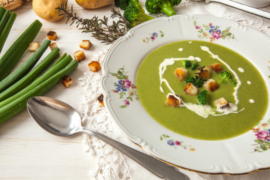 Spring detox broccoli green cream soup with potatoes and vegan cream in bowl on bright wooden board over white background, top view. Clean eating, dieting, vegan, vegetarian, healthy food concept