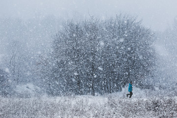 Young man jogging through meadow pathway during heavy snowing. Workout outdoors during winter snow...