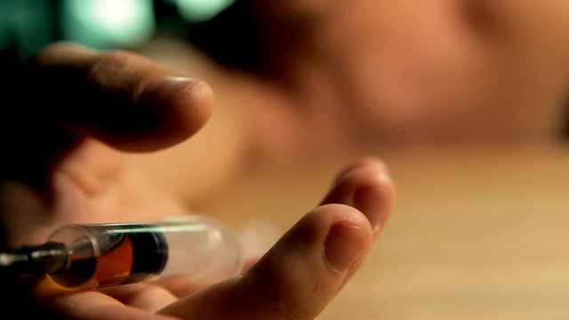 Hand Holding A Syringe .A man is a drug addict with a syringe using drugs. Close up.Concept