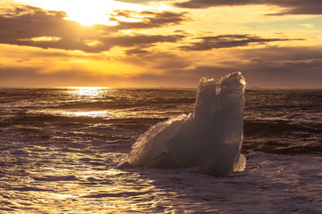 Fototapeta premium Ice cliff with a black sandy beach on Jokulsarlon beach (Diamond Beach) in southeast Iceland. Ice in the light of the rising sun