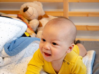 Cute 4 months old old mixed race Asian Caucasian boy looking happy smiling and laughing at the camera, tummy time on belly on the bed, healthy child baby boy. Half Thai half Polish.