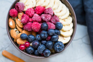 Muesli bowl with berries, banana and almonds, oatmeal breakfast bowl top view with raspberries and blueberries