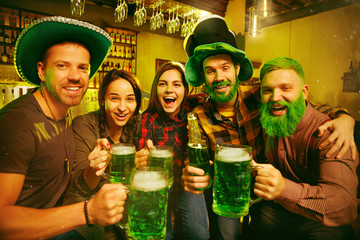 Saint Patrick's Day Party. Happy friends is celebrating and drinking green beer. Young men and women wearing a green hats. Pub Interior.
