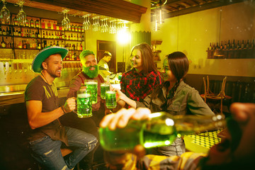 Saint Patrick's Day Party. Happy friends is celebrating and drinking green beer. Young men and women wearing a green hats. Pub Interior.