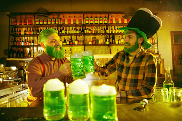 Saint Patrick's Day Party. Happy friends is celebrating and drinking green beer. Young men and women wearing a green hats. Pub Interior.