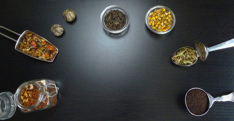 Tea assortment with tea flowers, green tea jasmine and chamomile at black wooden background