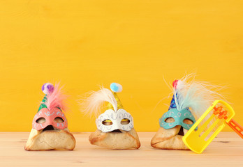 Purim celebration concept (jewish carnival holiday). Traditional hamantaschen cookies with cute clown hats and masks over wooden table.