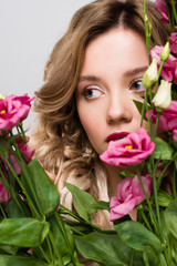 close up of beautiful spring young woman hiding behind Eustoma flowers isolated on grey