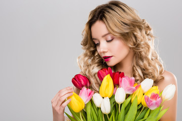 Obraz na płótnie Canvas young attractive spring woman looking at bouquet of colorful tulips isolated on grey
