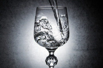 Clear transparent water pouring in to glass on grey background . Close-up .