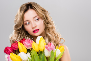 young attractive spring woman holding bouquet of colorful tulips and looking away isolated on grey