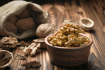 Walnut kernels in a clay bowl and a jute bag with whole nuts on the table