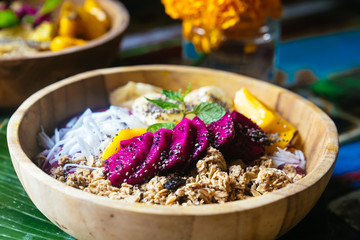 Close up four smoothie bowls made with mango, banana, granola, grated coconut, dragon fruit, chia seeds and mint on colored background