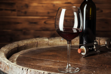 Bottle and glass of red wine on wooden barrel shot with dark wooden background