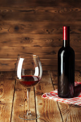 Glass and bottle with delicious red wine on table against wooden background