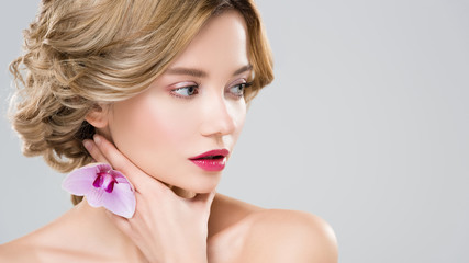 Naklejka premium young tender naked woman touching neck with purple orchid on hand isolated on grey