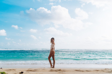 Fototapeta na wymiar Slim sexy girl in beige top and bikini posing on tropical beach