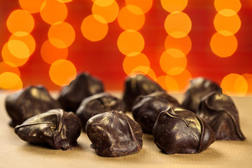 Close up of fresh, delicious and healthy homemade raw chocolate bonbons with golden sprinkles against red blurred background with lights bokeh
