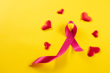 The text world cancer day and a pink ribbon on a yellow table background. The cancer, health, breast, awareness, campaign, disease, help, care, support, hope, illness, survivor and healthcare concept