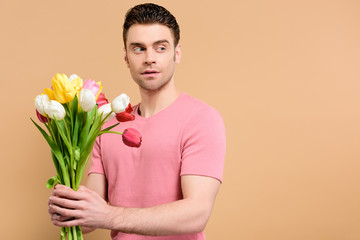 surprised man holding bouquet of tulips isolated on beige